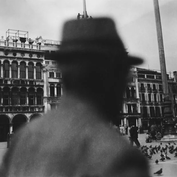Acerca de P.L.T. 7 Hombre con sombrero, de pie delante de un edificio.